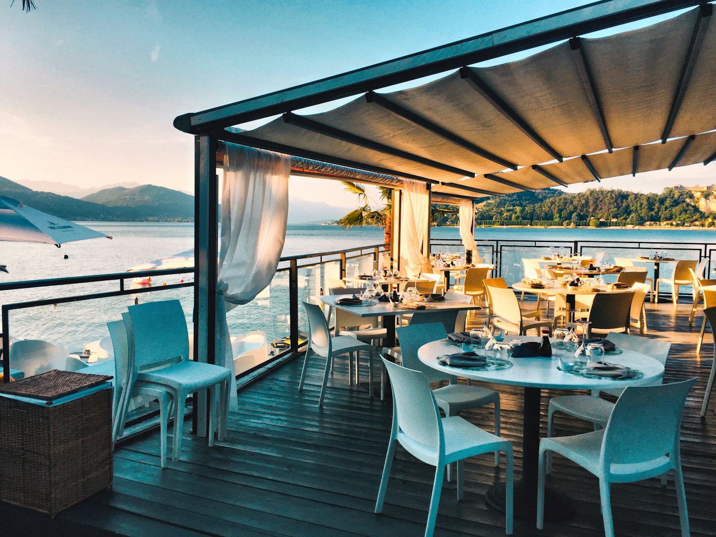 A curtained terrace table set for dinner above the water